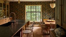 a cozy warm mustard and wood kitchen with wallpapered walls, a large kitchen island with a farmhouse wooden table
