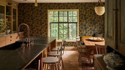 a cozy warm mustard and wood kitchen with wallpapered walls, a large kitchen island with a farmhouse wooden table