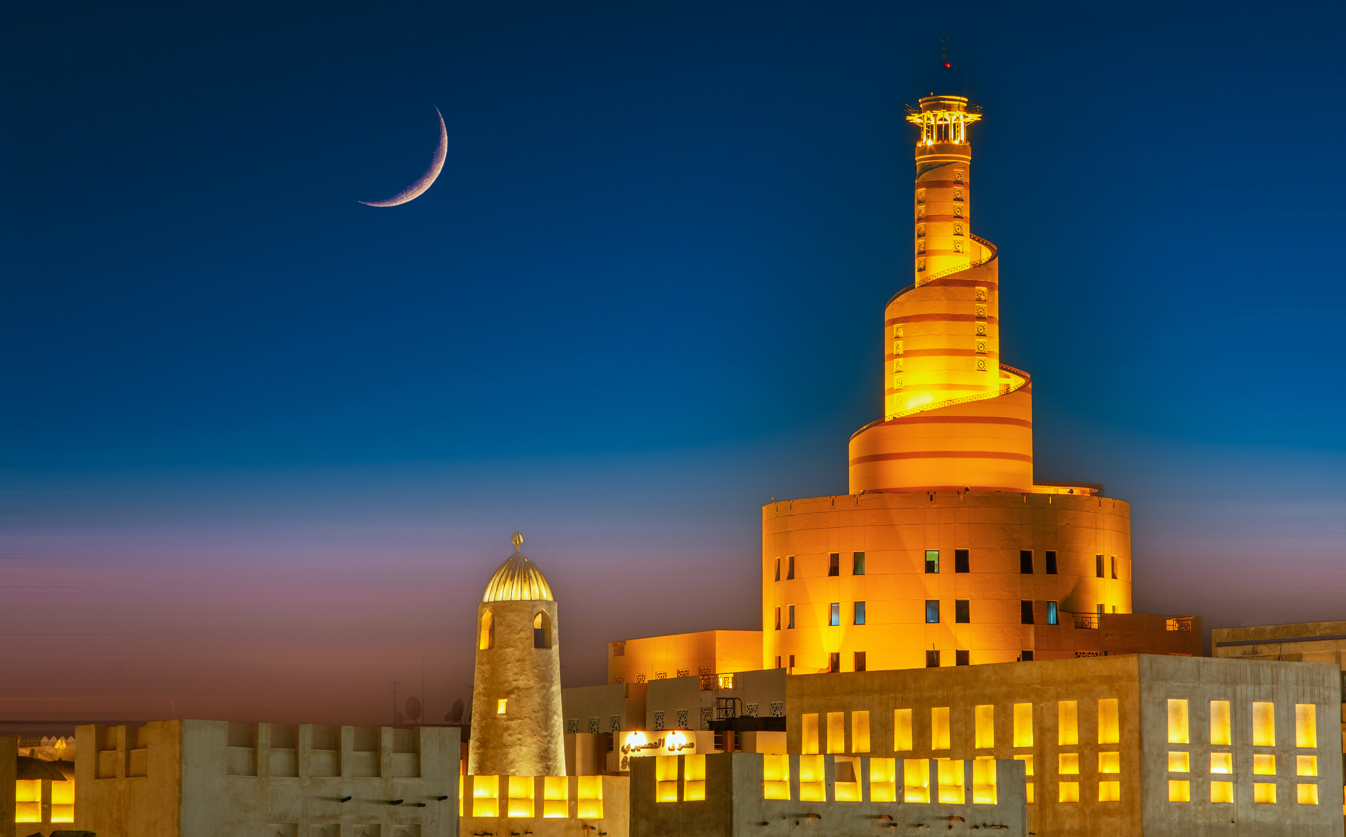 Qatar. The Illuminated Mosque Minaret of Al-Fanar Qatar Islamic Cultural Center with moon in the sky.