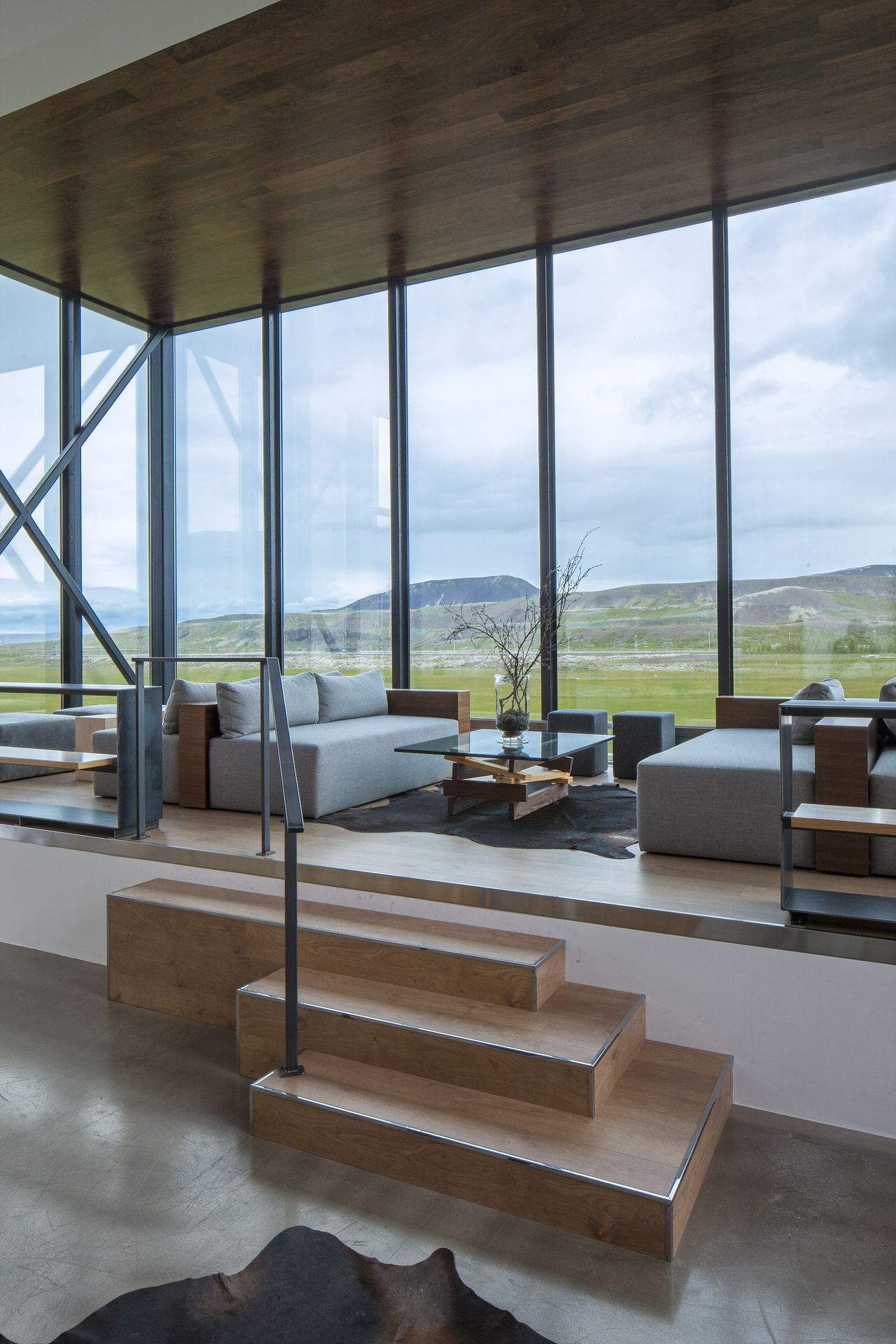 A hotel is nestled atop rocky formations in an Icelandic desert landscape, with floor-to-ceiling windows and minimal furnishings letting the outdoors in.