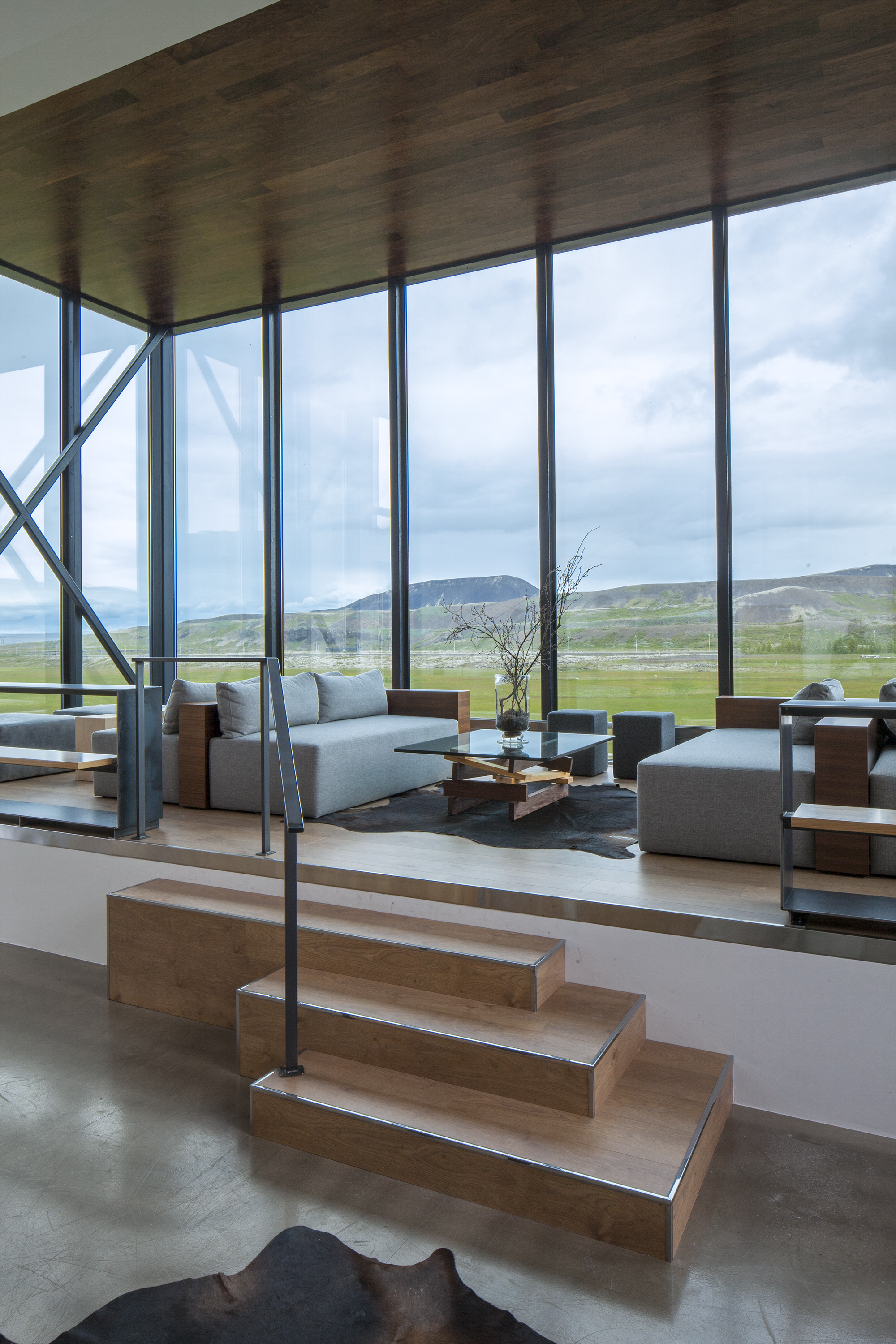 A hotel is nestled atop rocky formations in an Icelandic desert landscape, with floor-to-ceiling windows and minimal furnishings letting the outdoors in.
