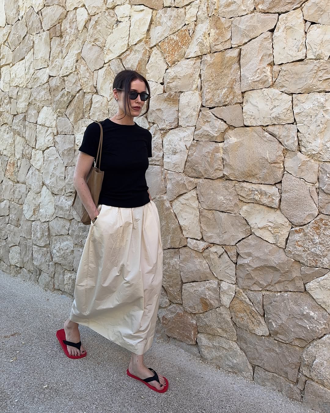 @annabelrosendahl wearing a white skirt, black t-shirt and flip-flops