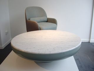 Grey single sofa next to a round marble coffee table on a white platform in a room with white floors and grey flooring