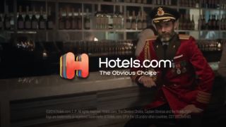 Brandon Moynihan sits at a bar in his Captain Obvious uniform for Hotels.Com.