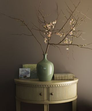 brown wall with side table with vase of branches and decorative objects