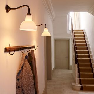 A white hallway with staircase with striped runner and lights and wooden coat hanger on the wall