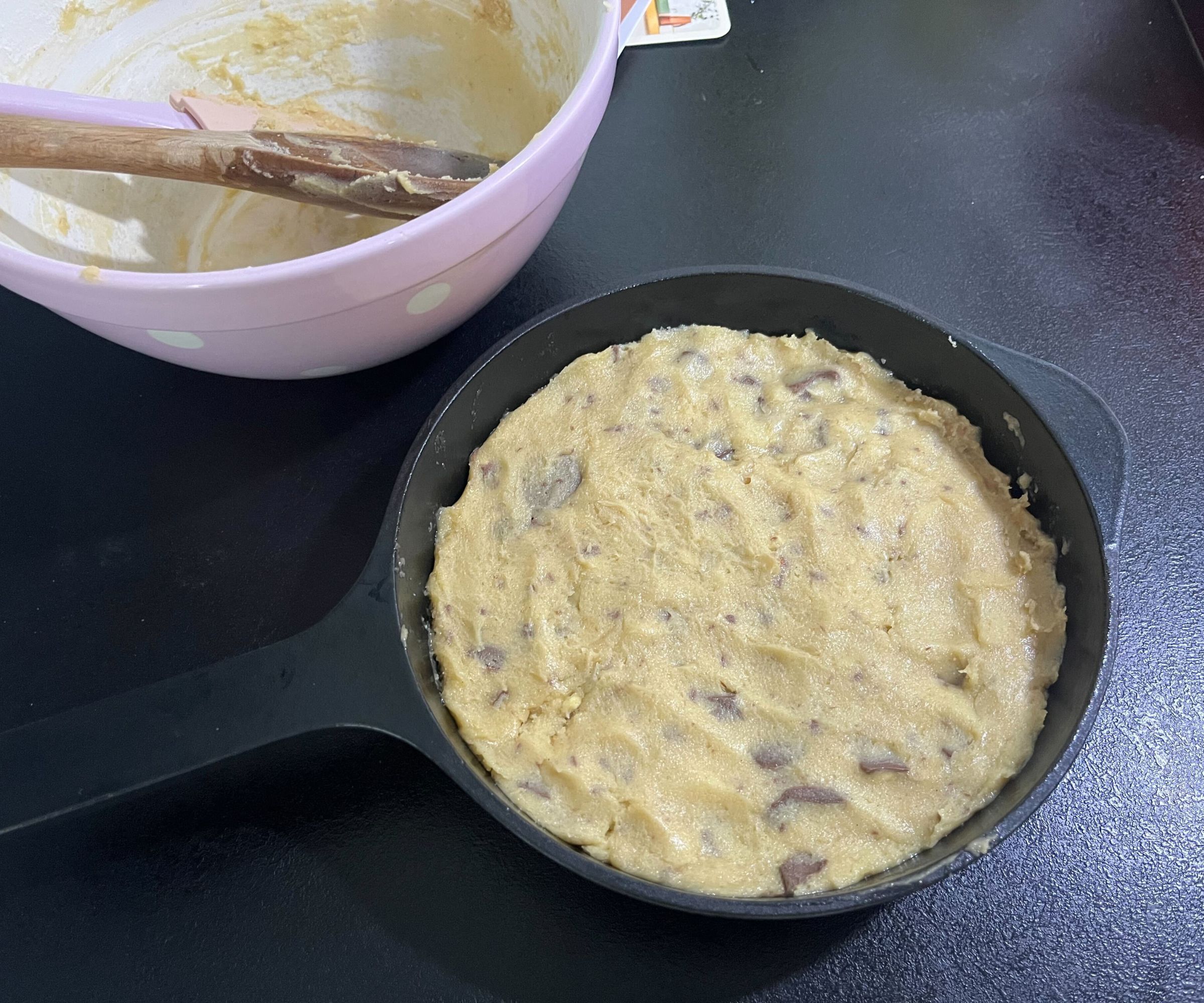 Cookie dough in a black cast iron skillet on a black counter. 