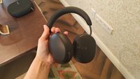 Black Sonos Ace Ultra headphones held over a brown wooden table.