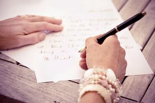 Person writing letters with black pen and white paper.