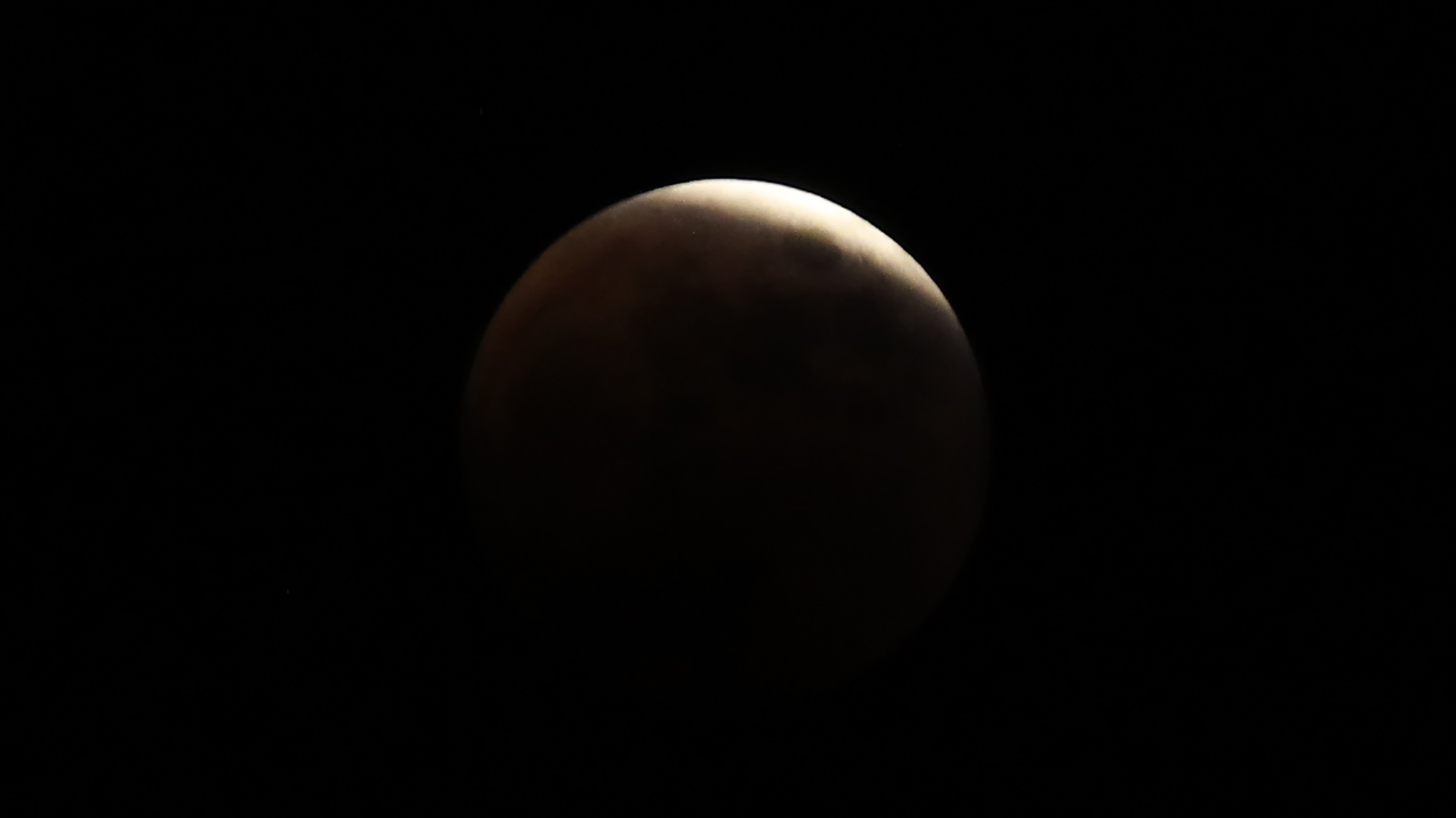 a barely illuminated moon with just one little bright sliver of light at the top