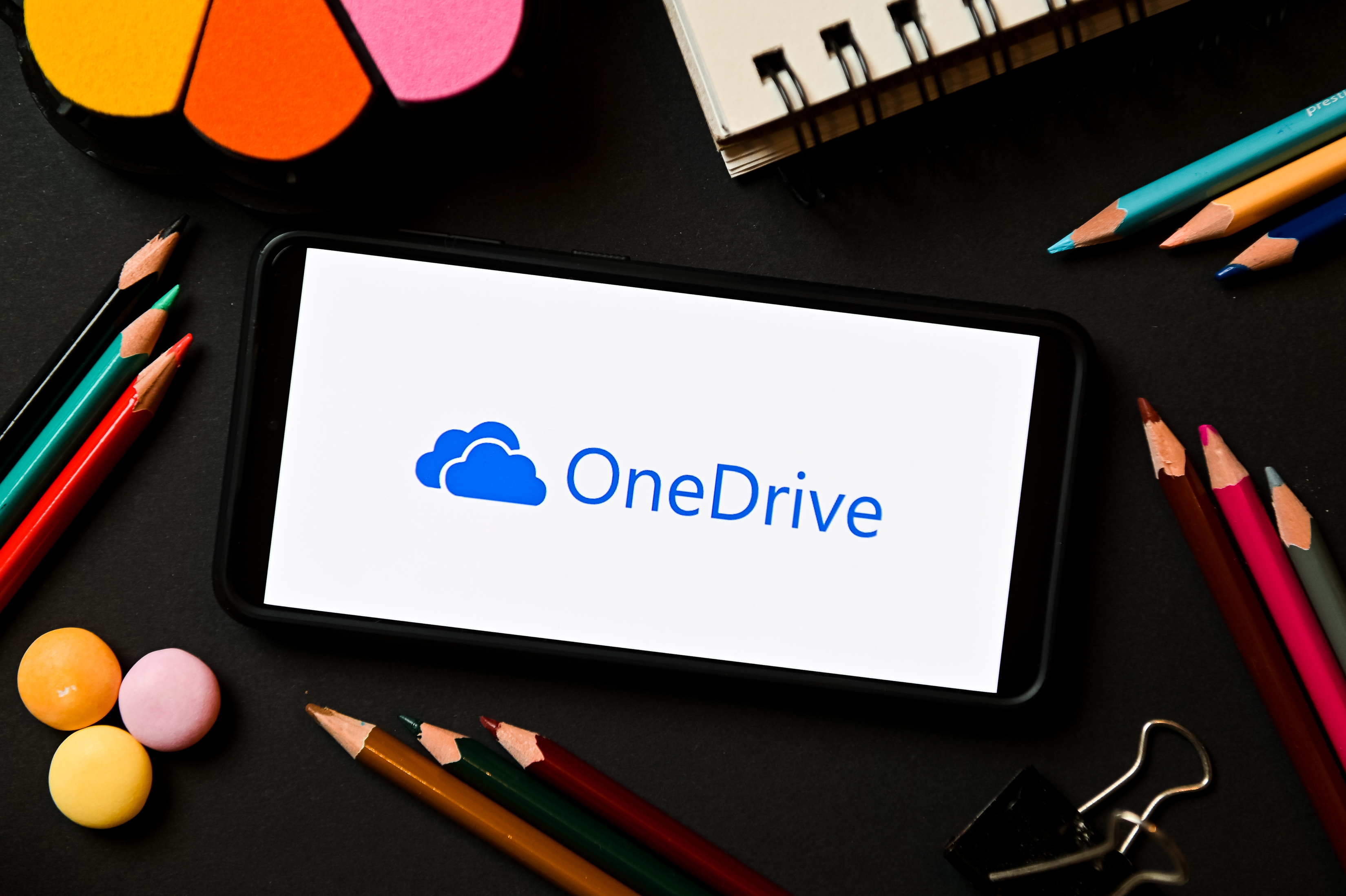 لوگوی OneDrive روی گوشی هوشمند در مقابل دستگاه ثابت