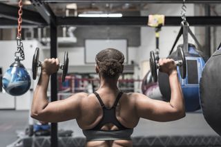 Black woman lifting dumbbells in gymnasium