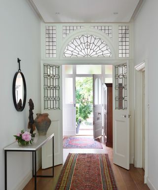 an all-white hallway with an open front door, and a side table, and mirror on the wall