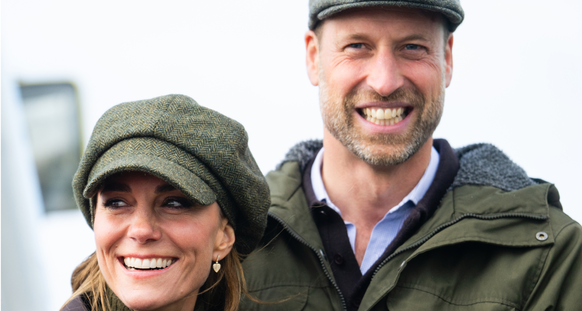 Princess Kate and Prince William smiling and wearing flat caps