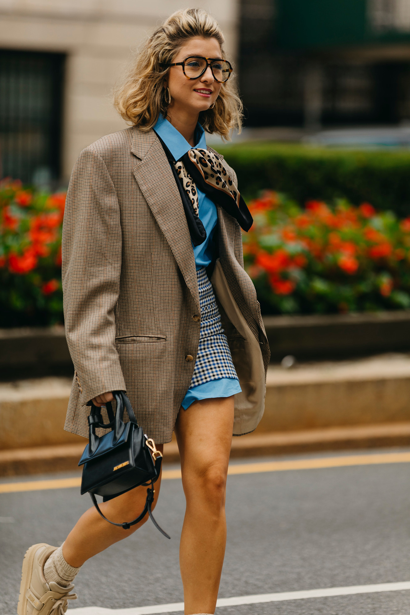A woman at New York Fashion Week wearing a cheetah print silk scarf with a blue shirt dress, mini skirt, and brown blazer