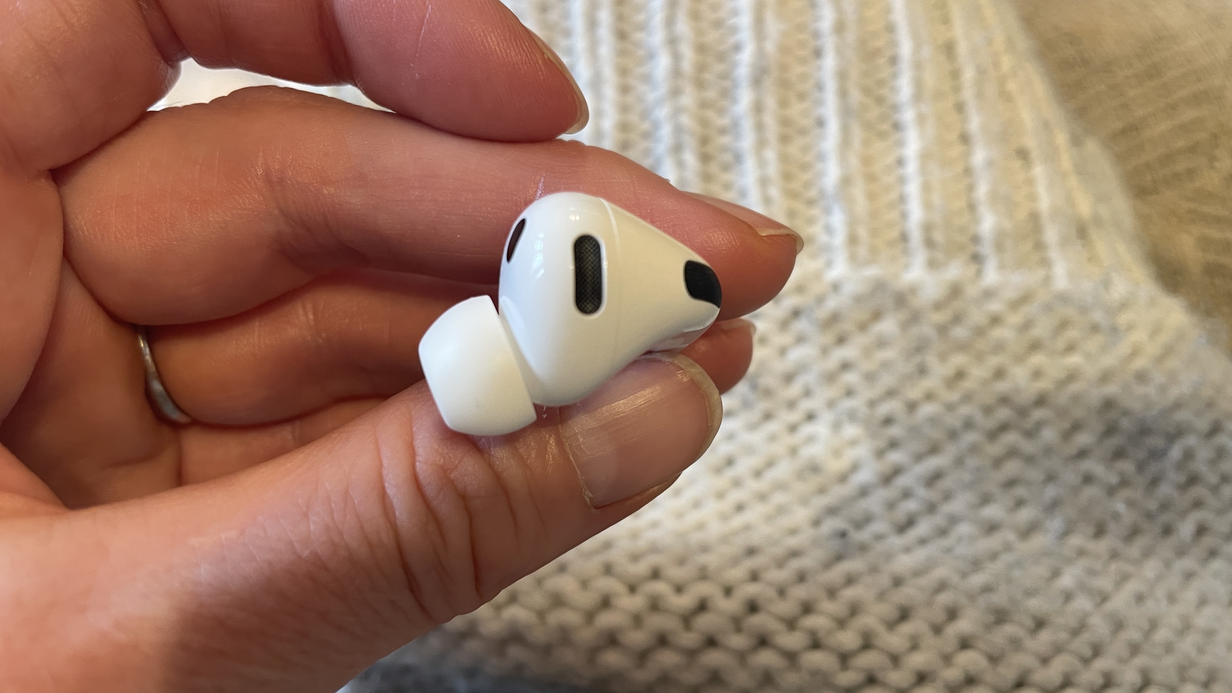 Apple AirPods Pro 3 held in a hand, with beige woollen background