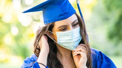 A college graduate wears a face mask and a cap and gown