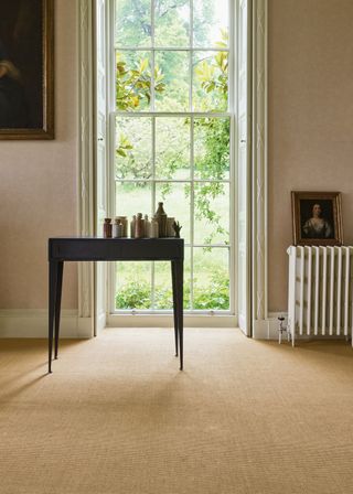 Cream colored carpet, with a table on top of the carpet. There is a radiator in the corner of the room with a picture on top.