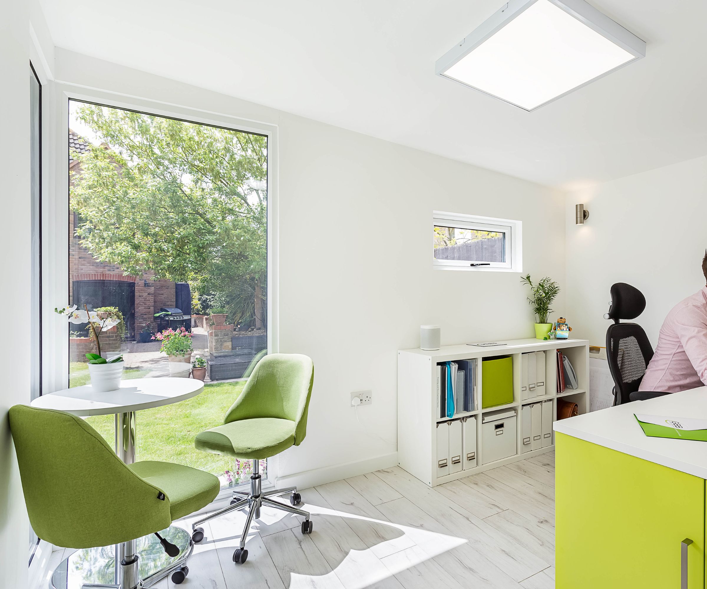 A bright garden sun room with a home office inside, two green swivel chairs and a bright green desk