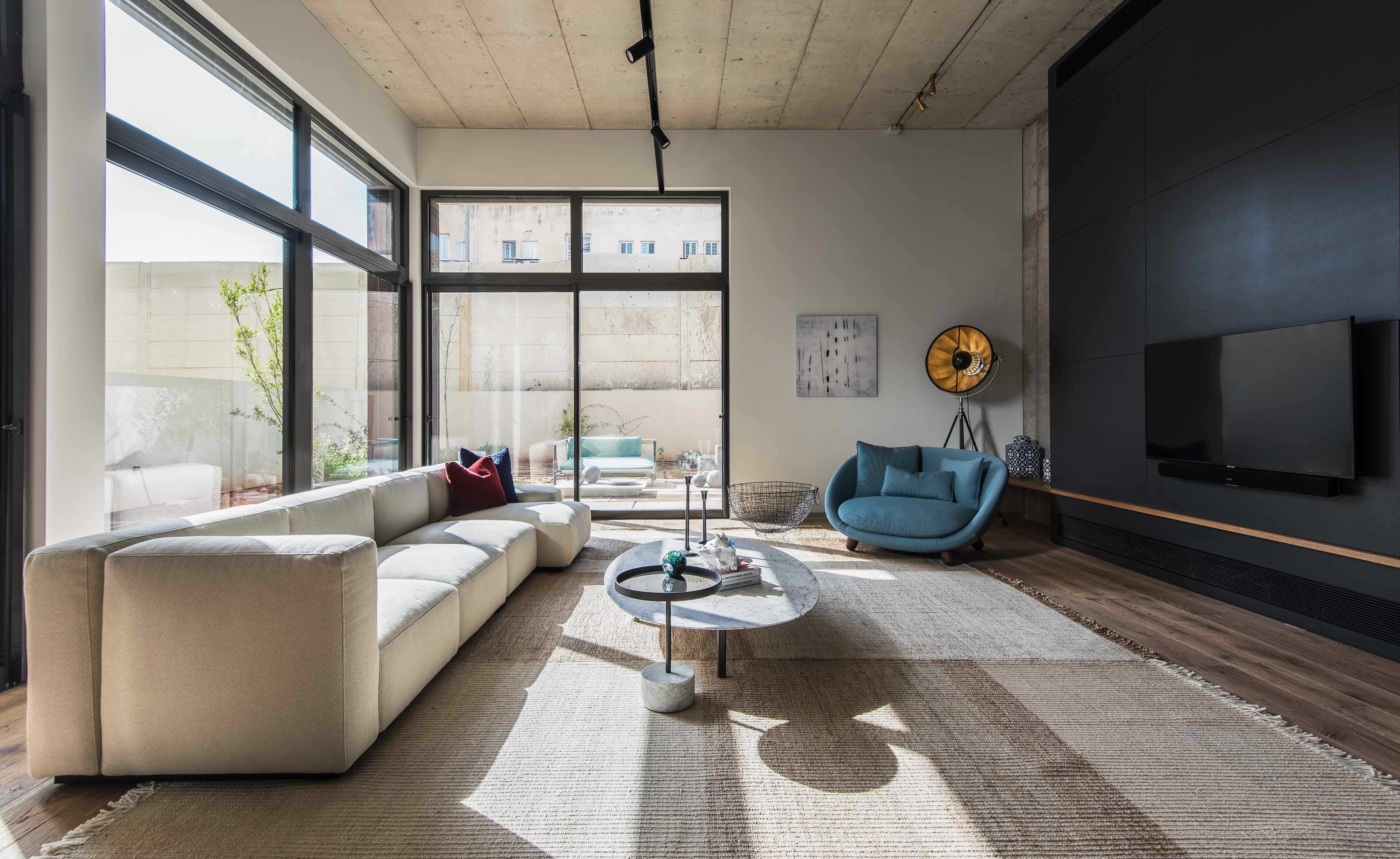 Large lounge area with l-shaped sectional, coffee table, designer couch, dark feature wall with television, wrap around glass windows look out onto patio