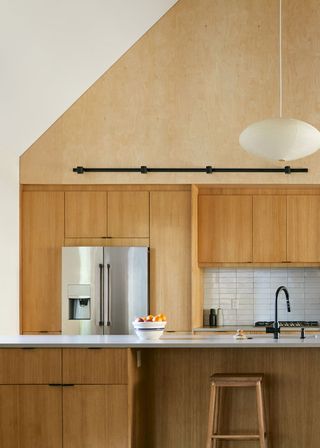 A sleek and timeless kitchen with wooden textures. A bar stool is placed by the kitchen island as well as a light pendant with shade above it.