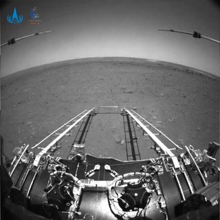 This black and white view of Mars is a photo from a navigation camera on China's Mars rover Zhurong released on May 19, 2021 about 4 days after landing. The ramp to the Martian surface from Zhurong's lander is visible, as are two subsurface radar instruments on the rover and the Martian horizon in the wide-angle view.