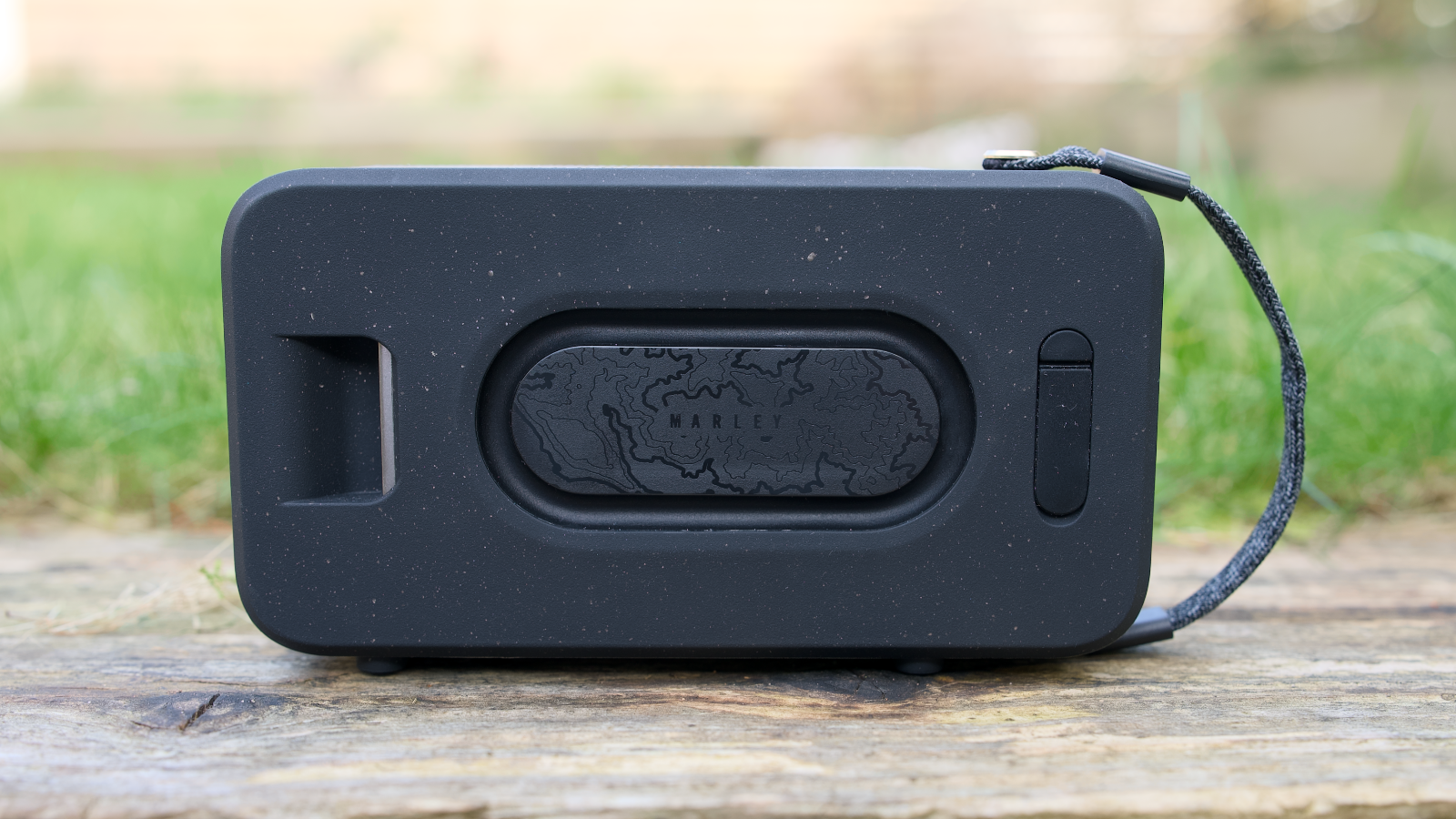 House of Marley Roots Solar Bluetooth speaker outdoors in a garden, on a wooden bench.