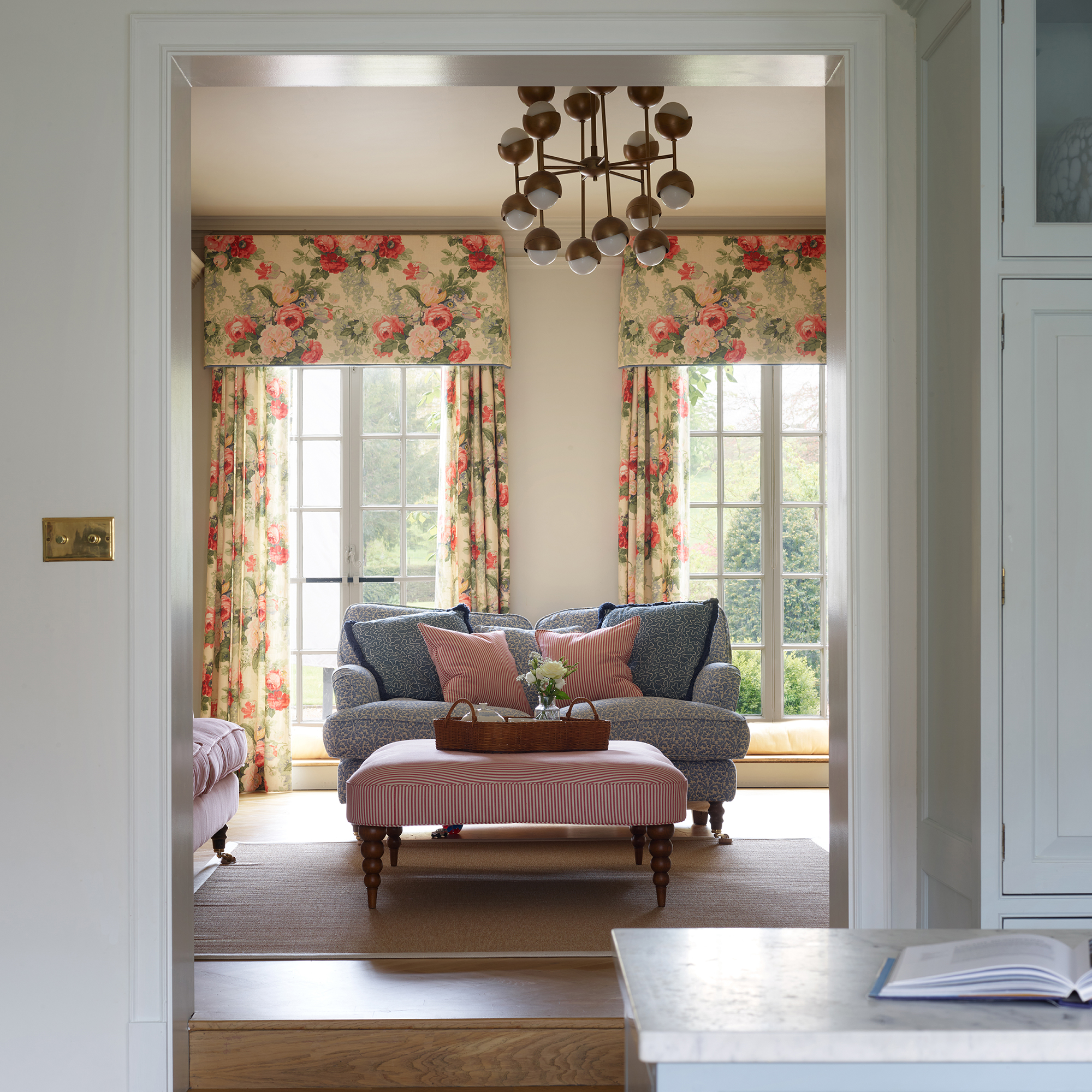 snug off a kitchen with floral curtains and pelmet, blue sofa and pink footstool