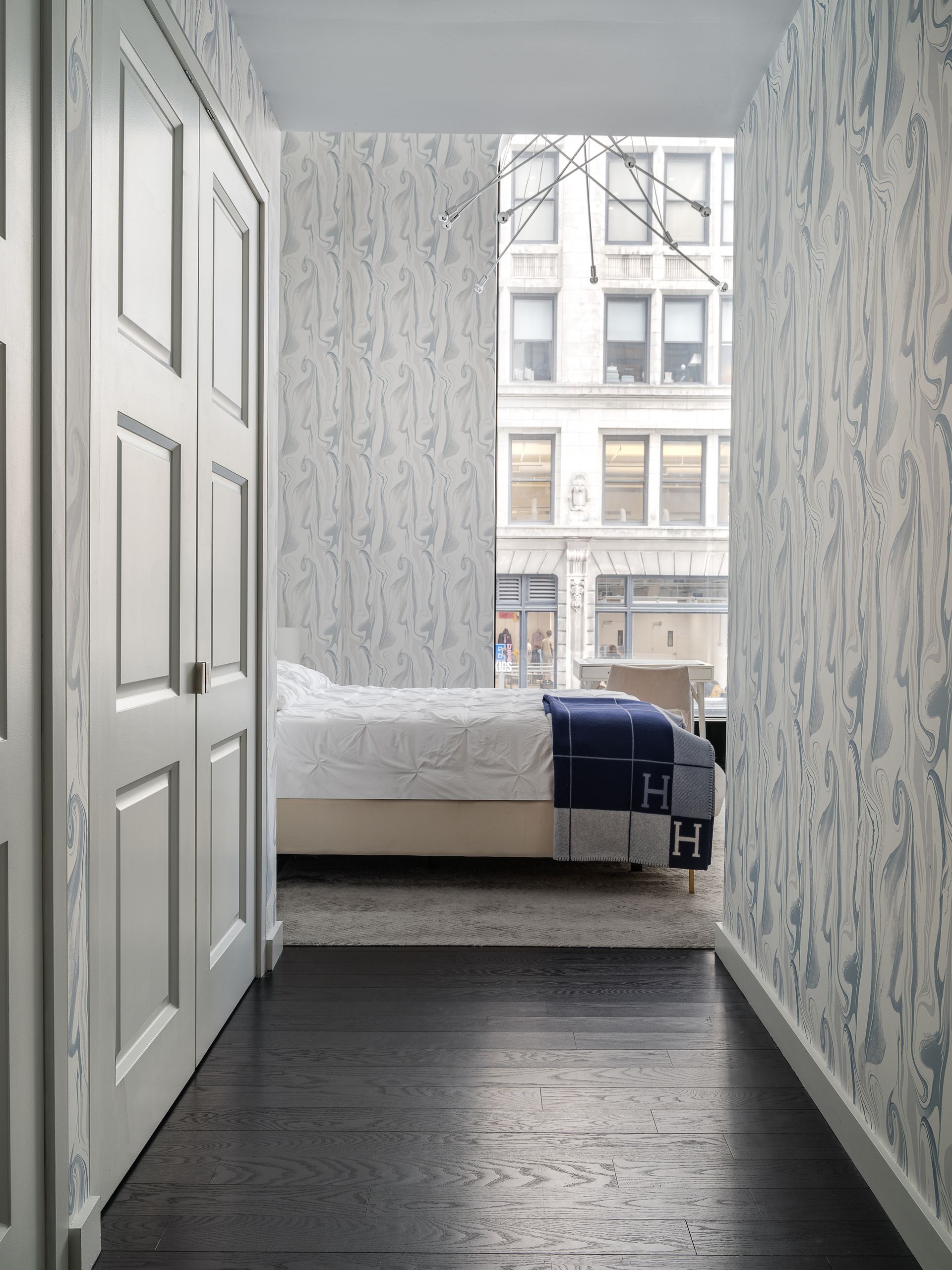 A wallpapered bedroom with window, bed and cupboard