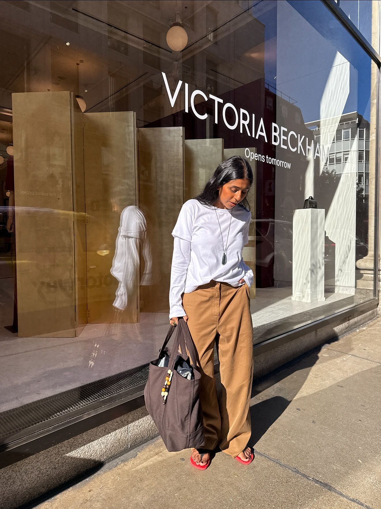 An image of @monikh wearing the double shirt trend, one of the biggest trends making a comeback for winter 2025, with The Row Dune flip-flops and camel trousers.