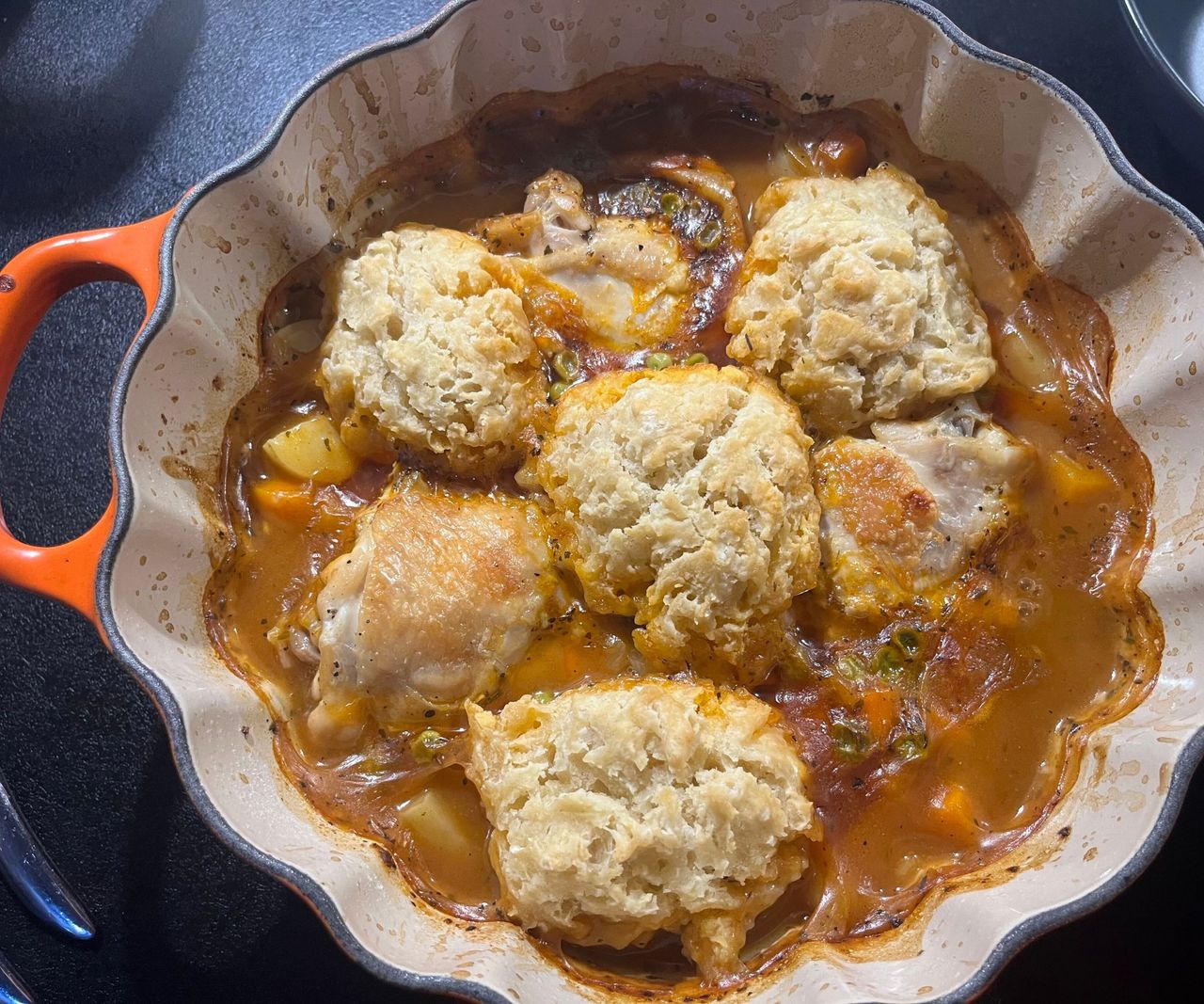 An orange Le Creuset Pumpkin cocotte on a black kitchen counter with a stew and dumplings inside.