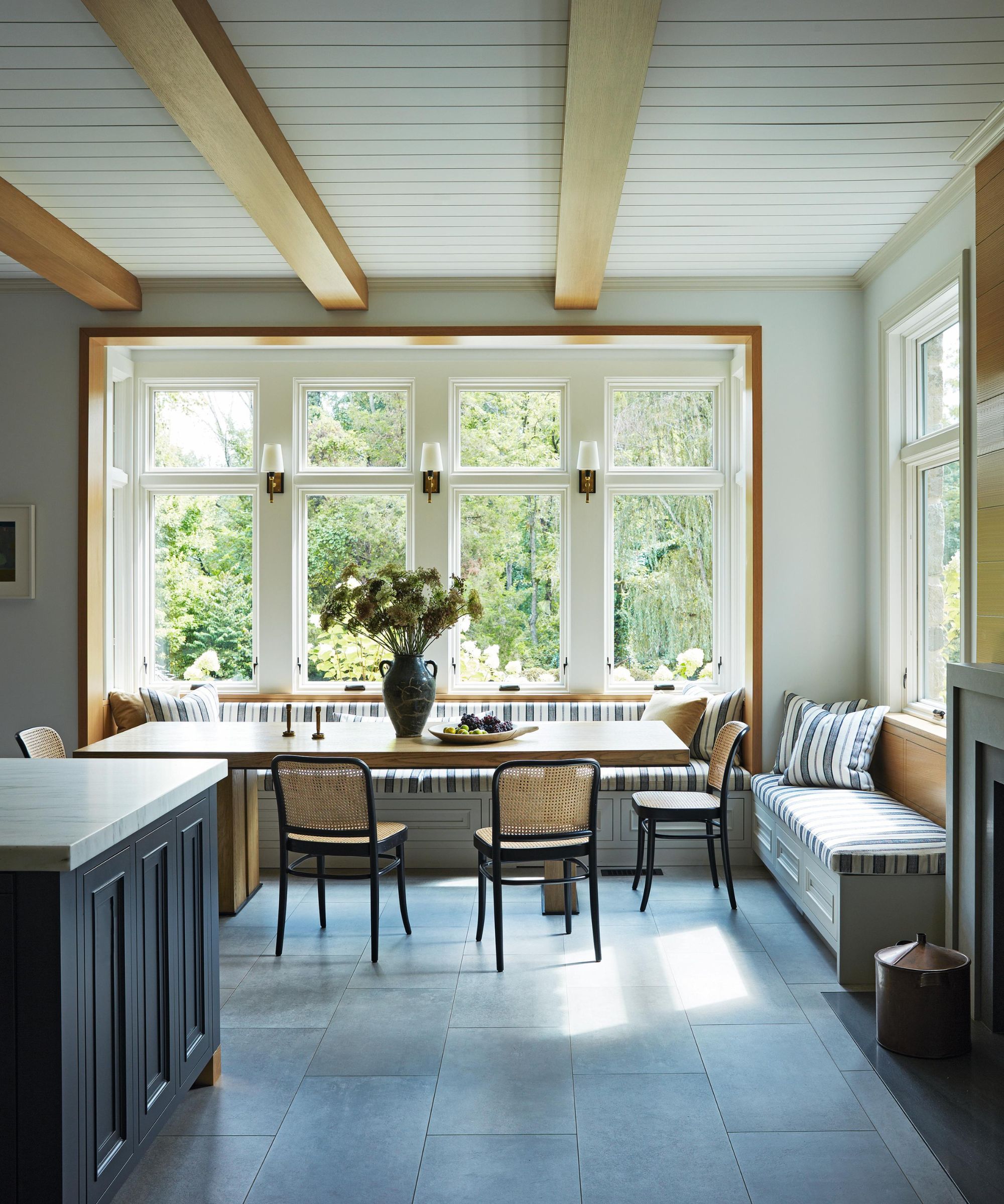 a light and bright kitchen dining area with a striped large banquette, ceiling beams and blue tiled floor