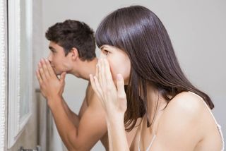 A man and a woman look at their skin in the mirror.