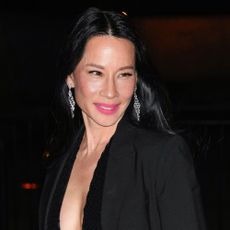 Lucy Liu smiles and looks away from the camera wearing pink lipstick