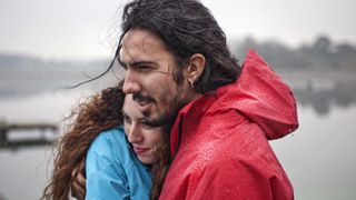 A man and a woman wearing waterproof jackets embrace in the rain