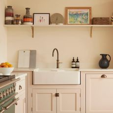 colour ideas for cottagecore decor, cottage style kitchen with blush cabinetry , white Butler sink, green range to the left, open shelving with artwork, clock and ceramics