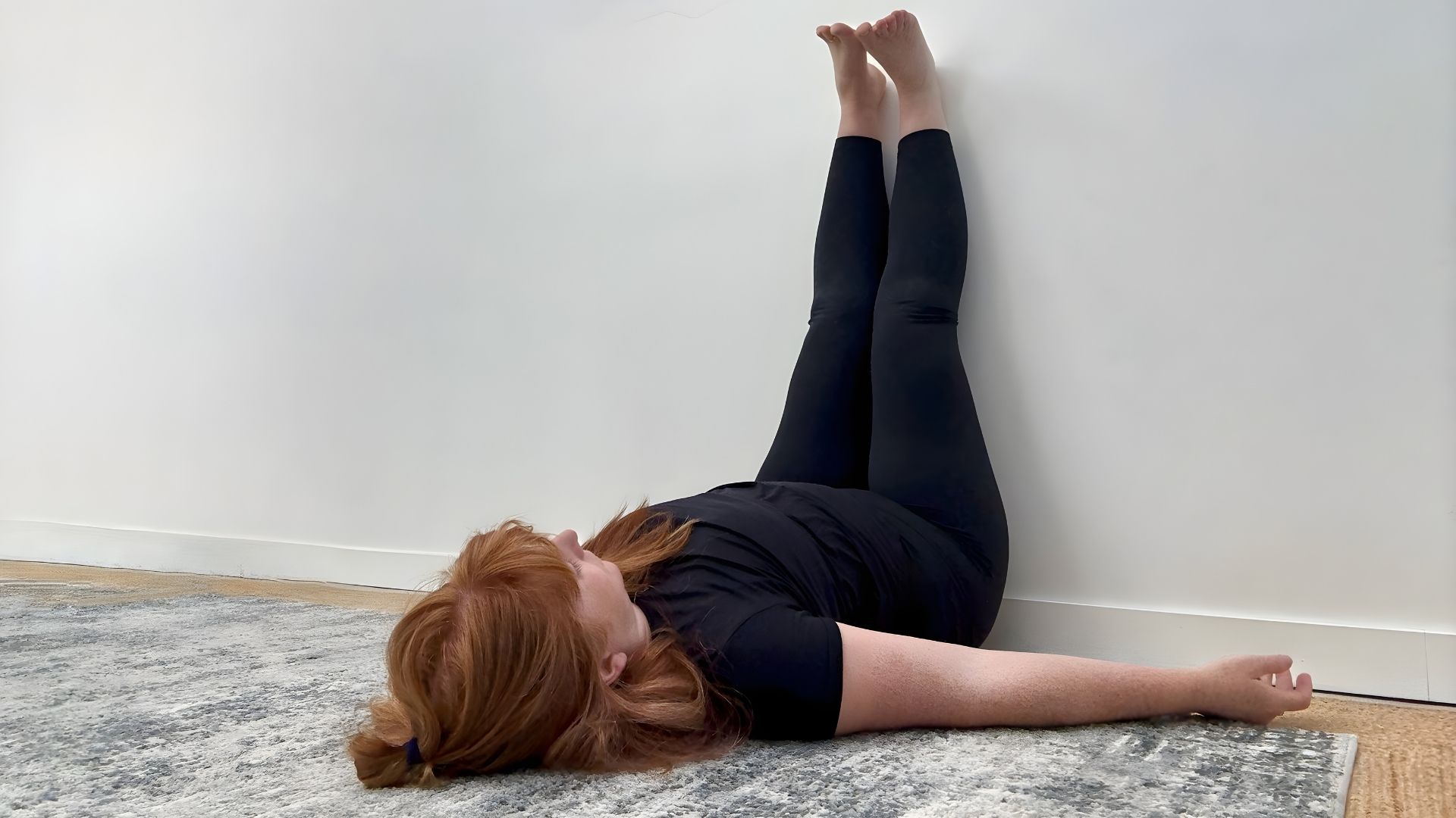 Woman in black clothing demonstrating legs up the wall yoga pose