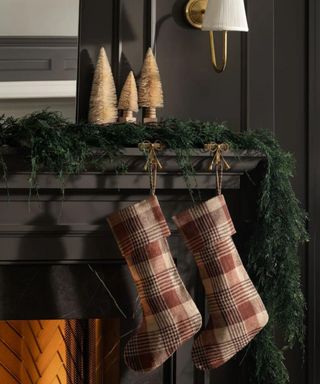 Stockings hanging from a garlanded mantel above a fireplace against a gray wall.