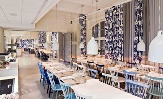 Aveqia dining room with long tables, blue and white wooden chairs, blue patterned curtains and large mirror on end wall