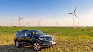 A Honda CR-V hybrid car is parked in a field next to wind turbines