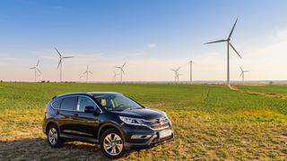 Une voiture hybride Honda CR-V est garée dans un champ à côté d'éoliennes.