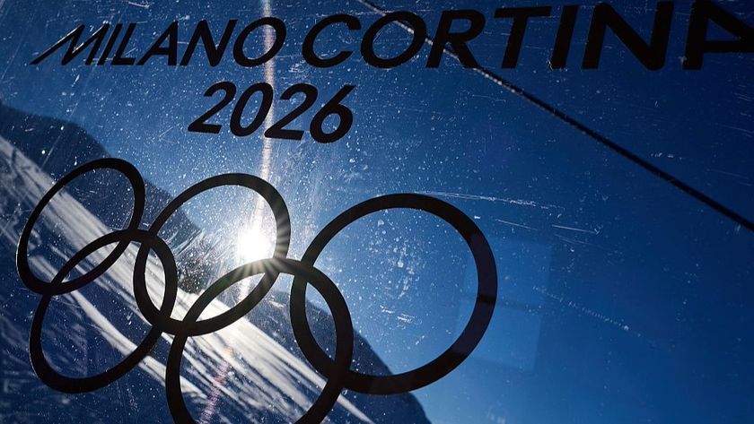 The Olympic rings on a perspex board beneath the 'Milano Cortina 2026' branding, with an alpine scene visible in the background.