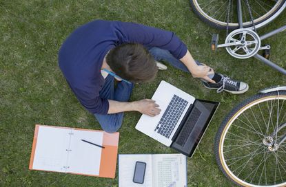 Overhead view college student studying with laptop grass