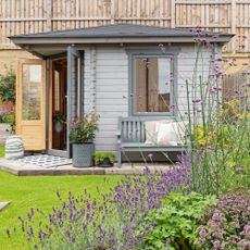 garden with summerhouse with doors open and a bench outside with a border in front filled with verbena and lavender