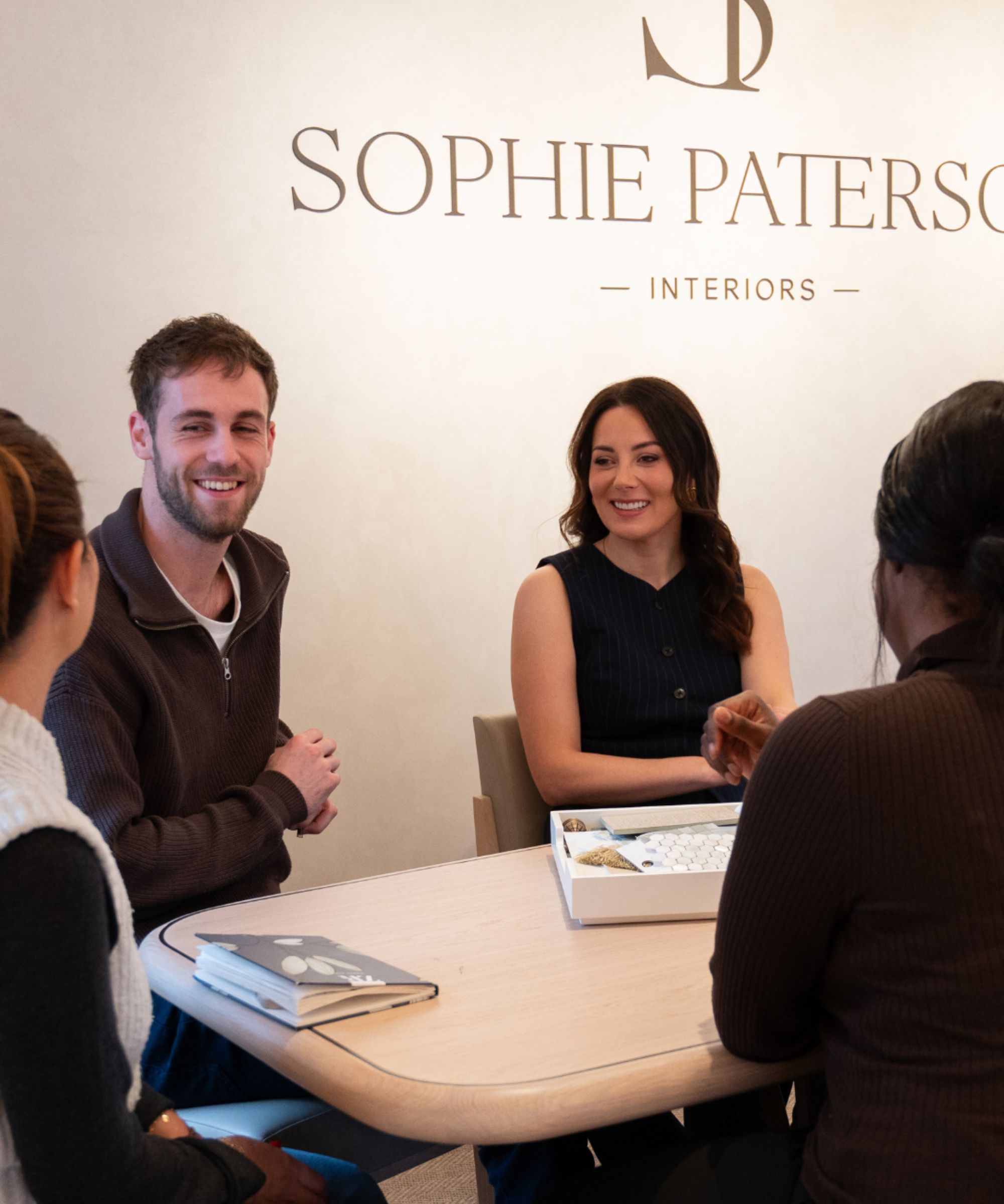 Sophie Paterson and others sat around a table, Sophie Paterson Interiors logo on wall behind