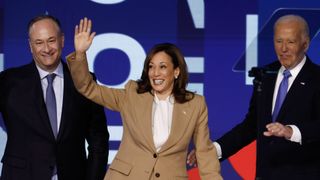 Kamala Harris, wearing a tan suit and flanked by Doug Emhoff and Joe Biden, waves to the crowd at the Democratic National Convention 2024