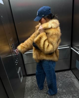 Fashion Influencer @Mimixn in New York is wearing an anti-trend outfit with an artificial pelza jacket, a New York Yanke's hat and relaxed Blue Jeans.