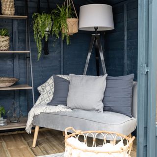 garden room with navy blue wooden wall grey sofa with cushions white lamp lights and wooden flooring