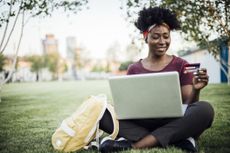 A student sitting on the grass in the park and looking at her student bank account