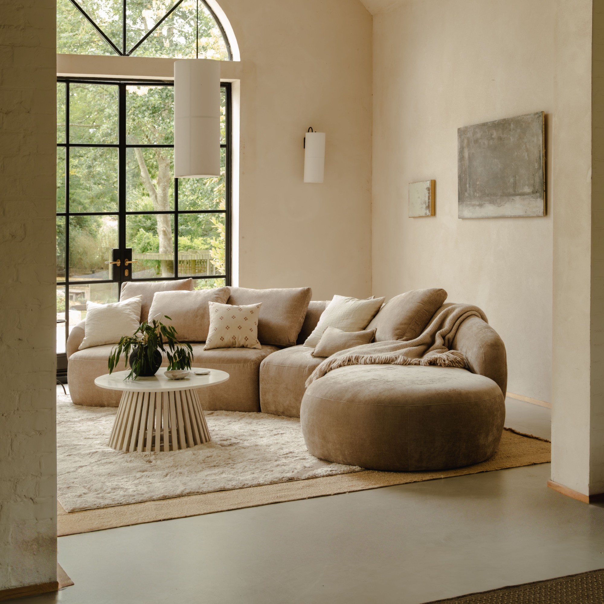 Aurelo&#039;s Curve chaise sofa in beige in a living room with high ceilings